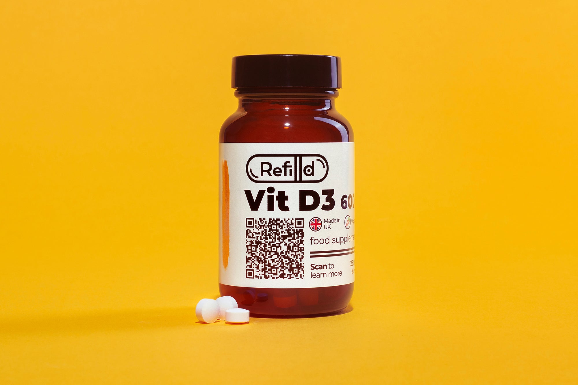 Refilld Vit D3 600 iu in a glass bottle with two tablets, yellow background. Vit D3, food supplement, yellow background