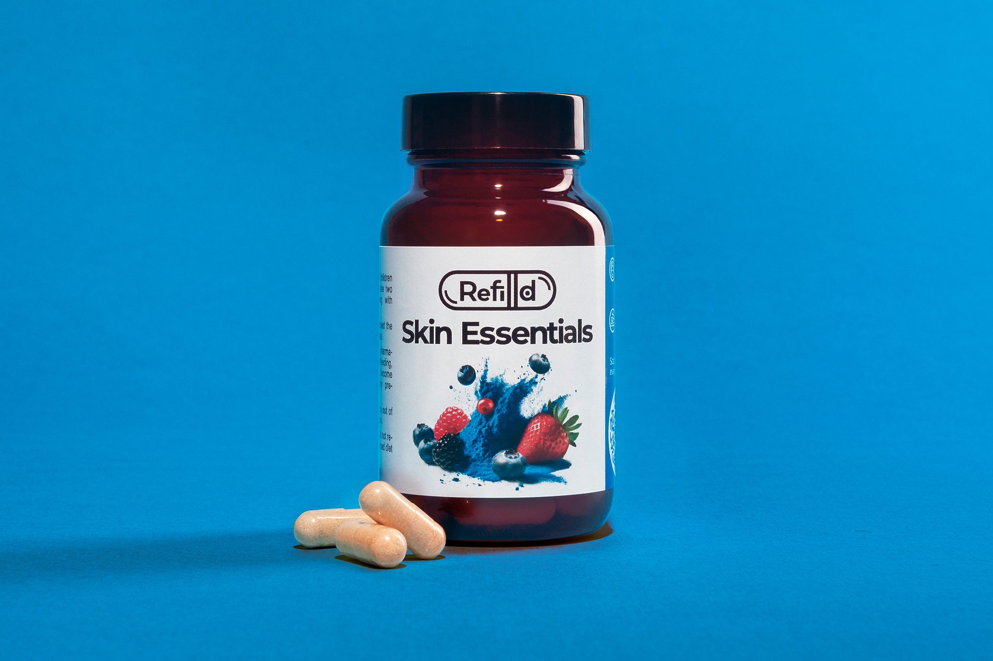 Refilld Skin Essentials bottle with capsules, featuring berry illustrations, placed on a blue background. Refilld Skin Essentials, food supplement, skin health, capsules, blue background, berry ingredients