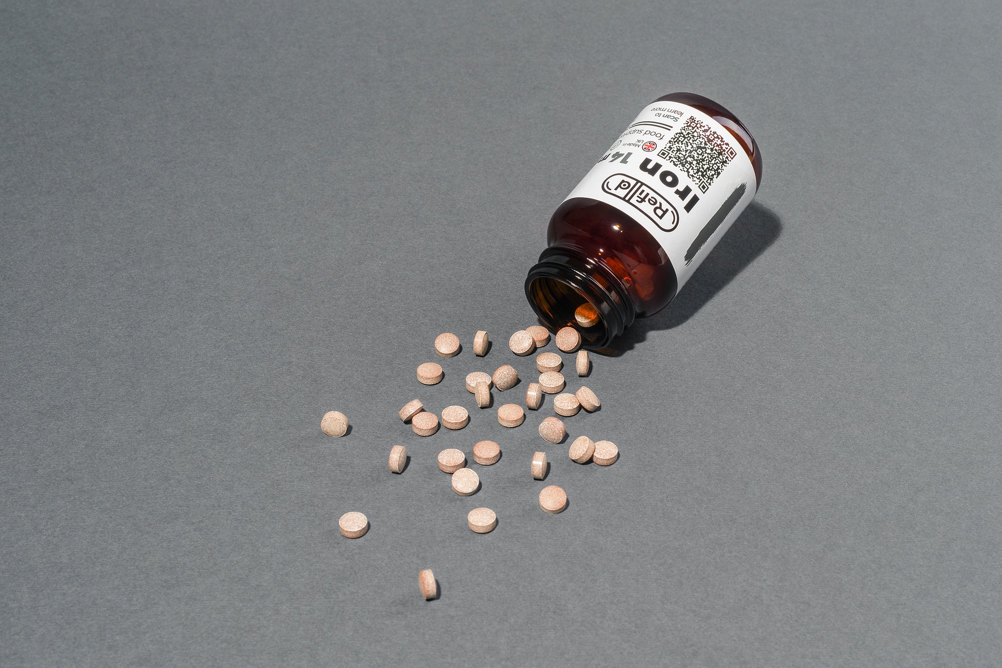 Refilld Iron 14 mg tablets spilled from the bottle on a gray background. Iron supplement, 14 mg, bottle, tablets, gray background.