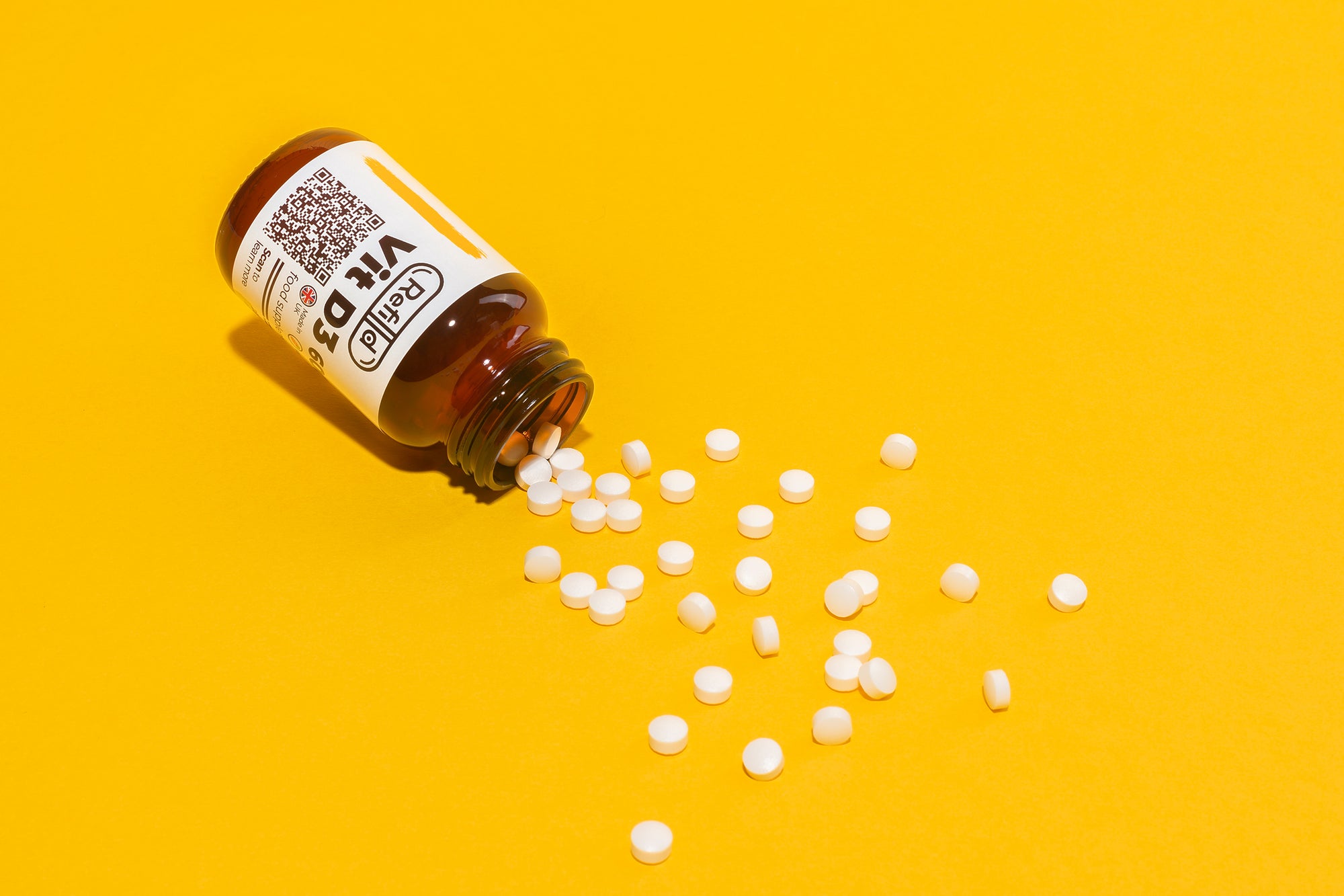 Refilld Vit D3 600 iu glass bottle spilling tablets, yellow background. Vit D3, tablets, yellow background