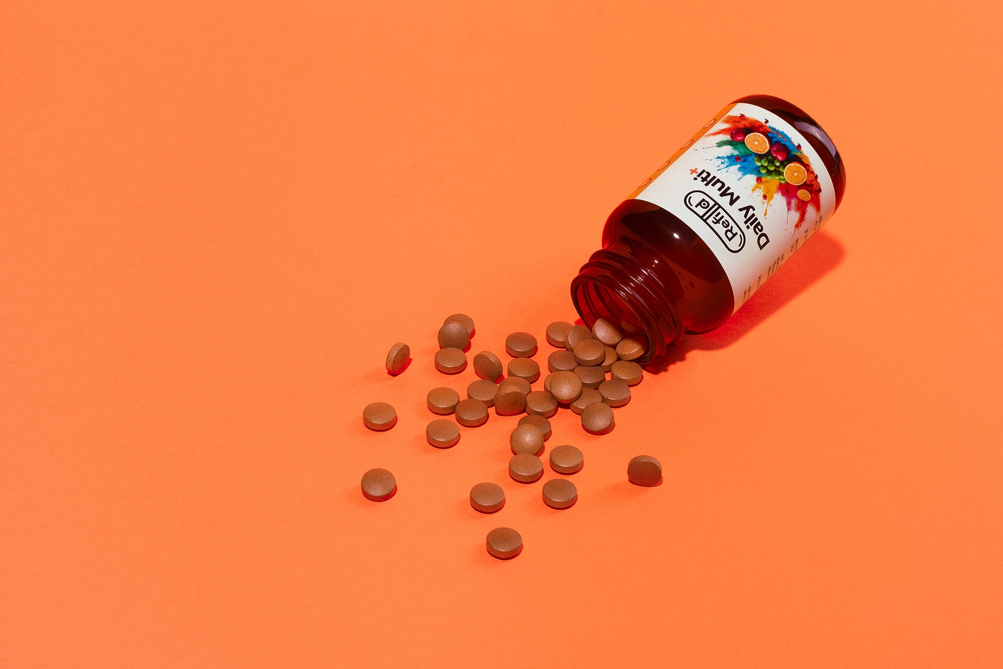 Spilled Refilld Daily Multi+ bottle with scattered tablets, shown on an orange background. Refilld Daily Multi+, food supplement, spilled tablets, vitamins, orange background