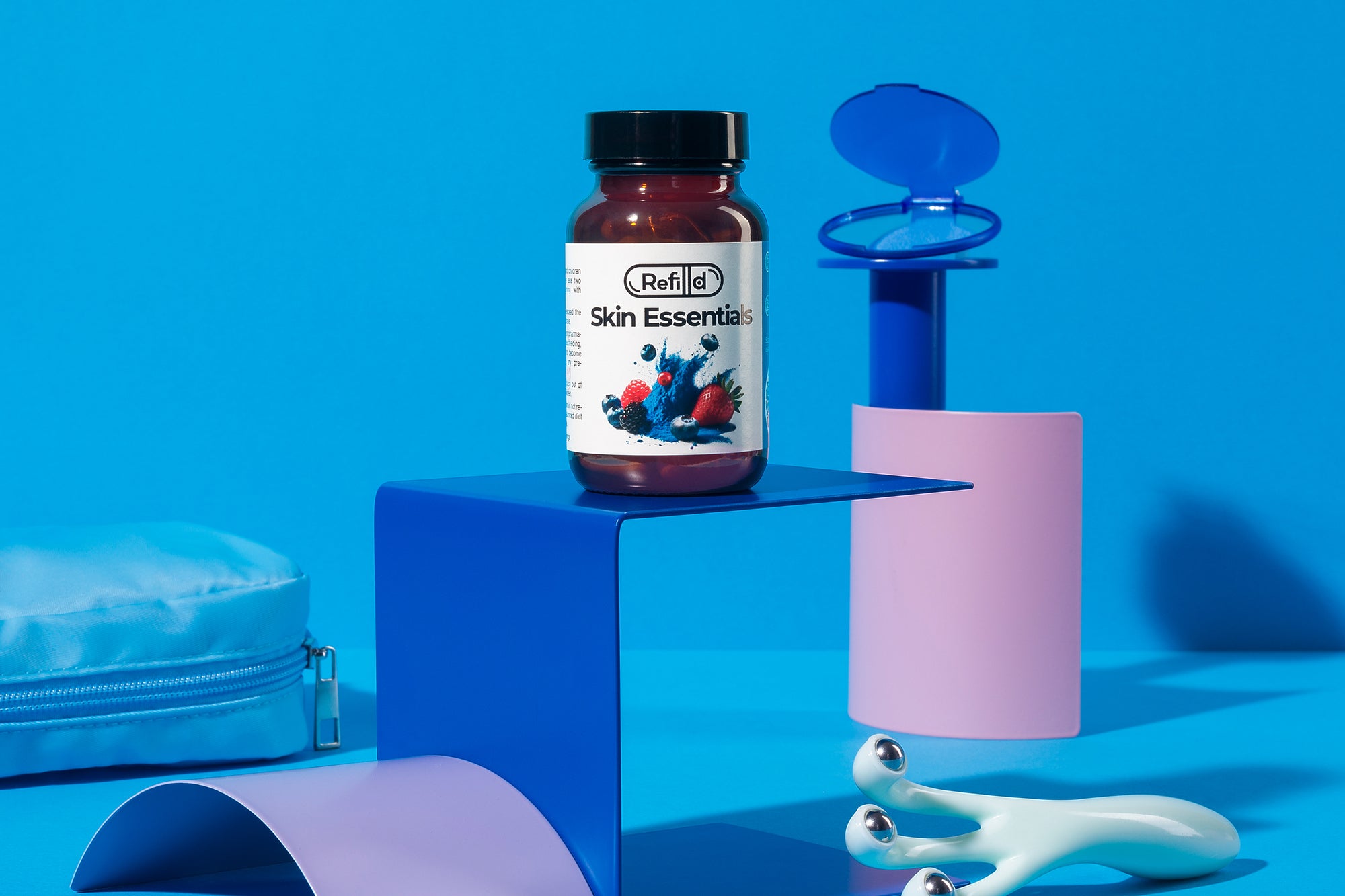 Refilld Skin Essentials vitamin bottle alongside skincare tools on a vibrant blue background, emphasising  radiant skin support.