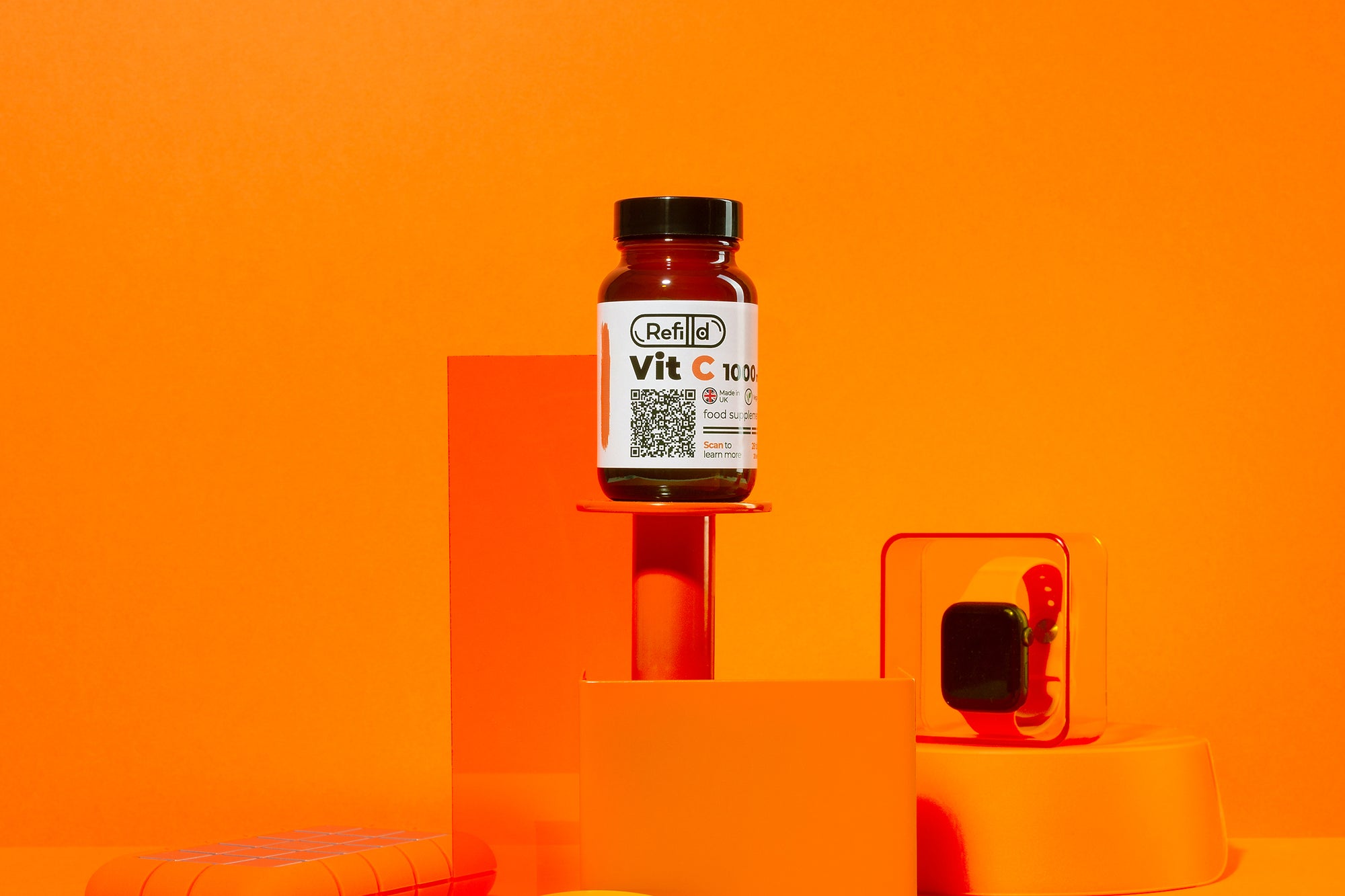 Refilld Vit C 1000 mg bottle elevated on orange geometric stands.
Refilld Vit C 1000 mg, food supplement, vitamin C, orange background, geometric display, immunity support