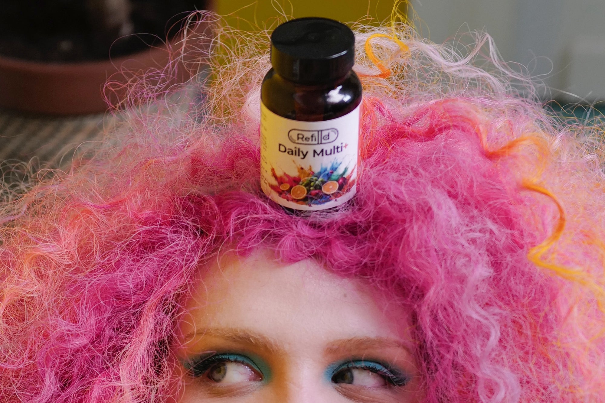 Rosie with pink curly hair balancing Refilld Daily Multi+ bottle on her head. Refilld Daily Multi+ supplement, fun marketing character.