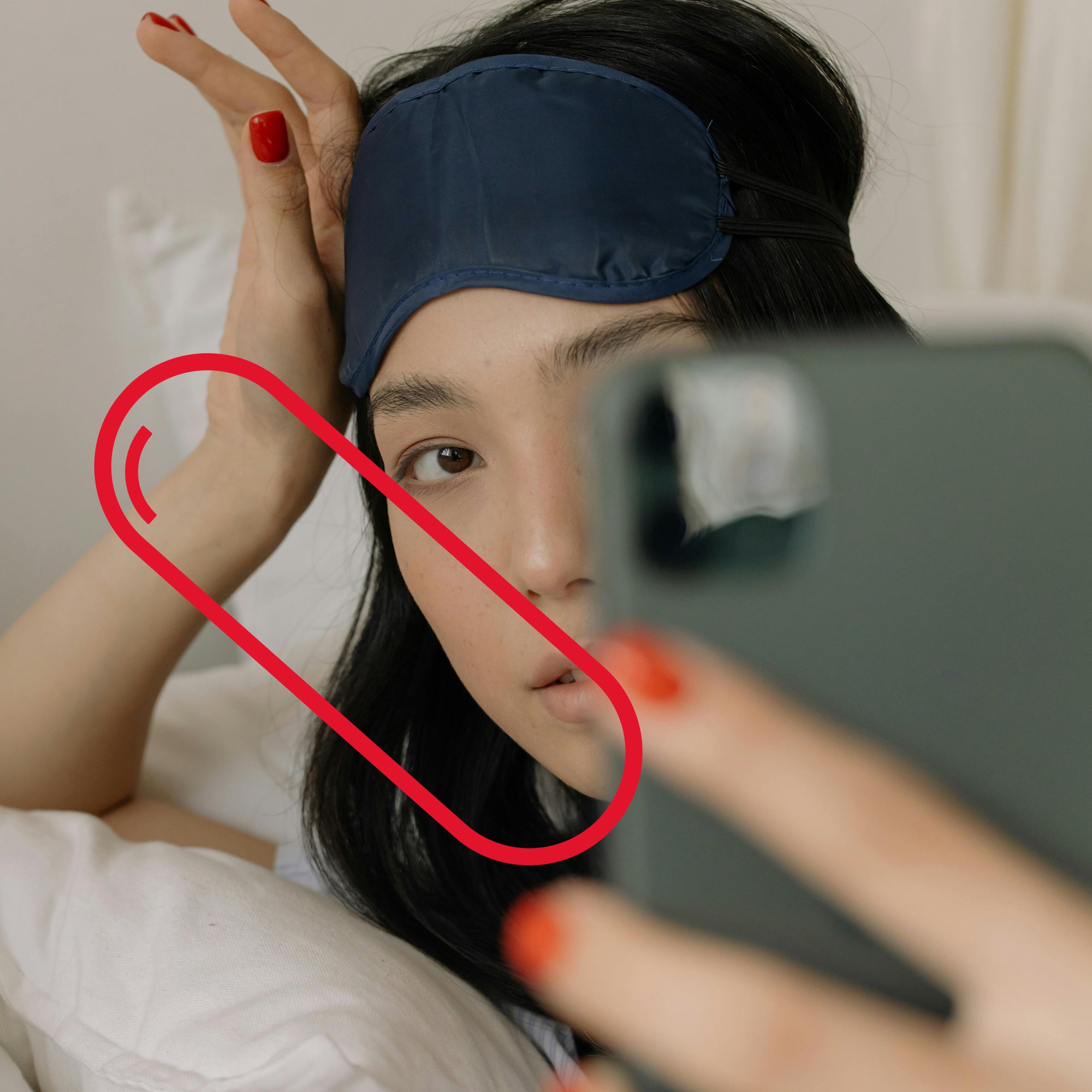 A person with a sleep mask checking their phone in bed. Vitamin A supports skin and eye health, bedtime routine.